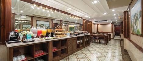 A hotel breakfast area with a buffet setup, including a coffee station, fruit, and various food items.