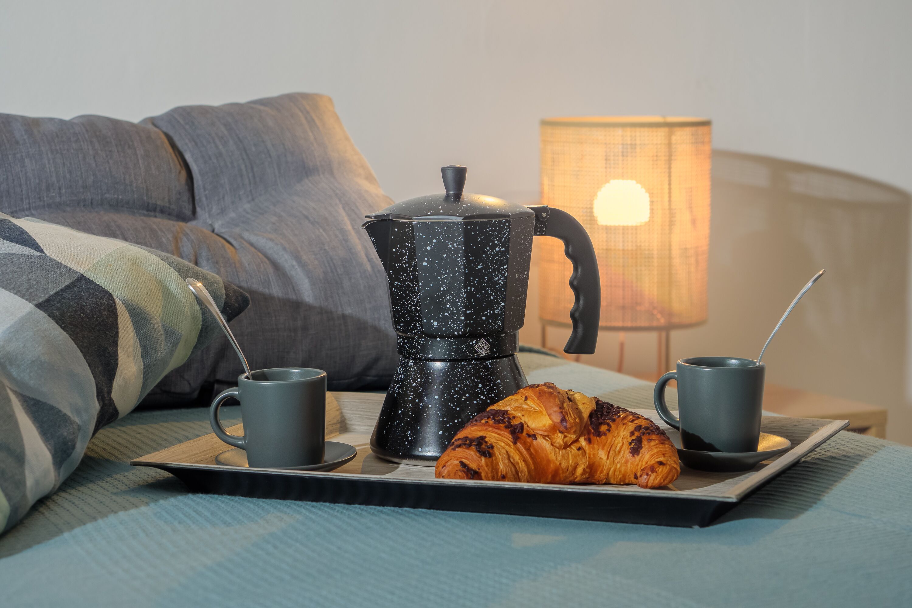 Un esmorzar agradable amb un croissant, dues tasses i una cafetera sobre un safata.