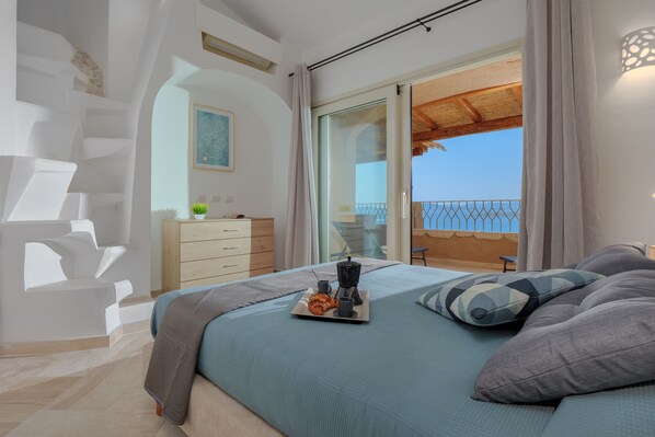A bedroom with a bed, a tray with breakfast items, a dresser, and a view of the balcony.