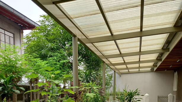 A covered outdoor area with a concrete bench, potted plants, and a seating area with chairs and tables. - Mang Ben Dormitory - Kaliraya QC - Hostel (Quezon City)