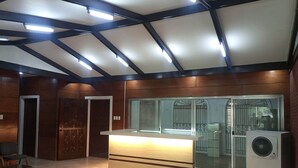 A reception area with a wooden reception desk, a washing machine, and a glass door leading to a balcony. - Mang Ben Dormitory - Kaliraya QC - Hostel (Quezon City)