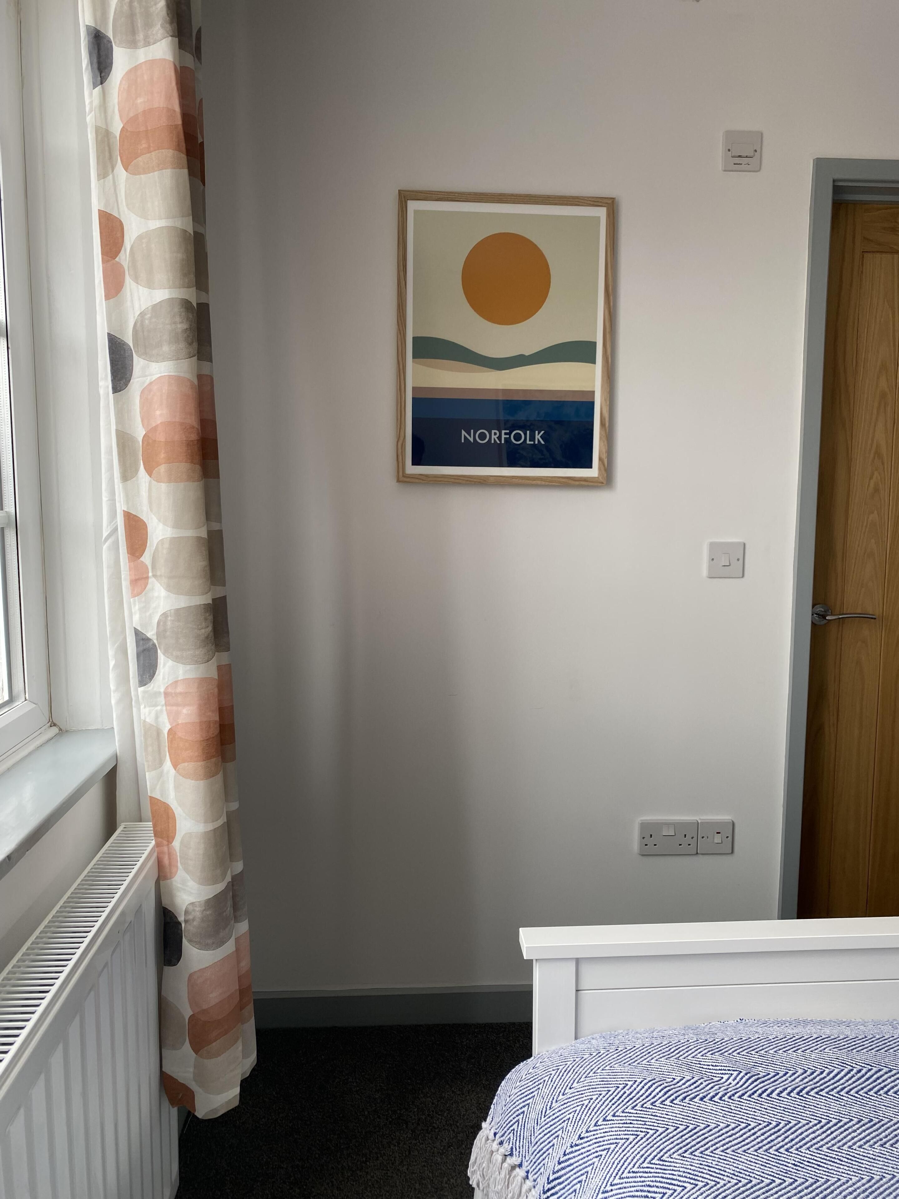 A room with a bed, a radiator, a curtain, a wall-mounted picture, and a door.
