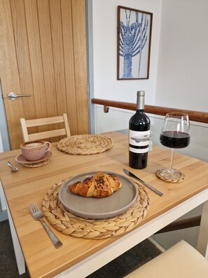 A wooden dining table with a plate of croissants, a bottle of wine, and a glass of red wine. - The Crows Nest - Sheringham (Sheringham)