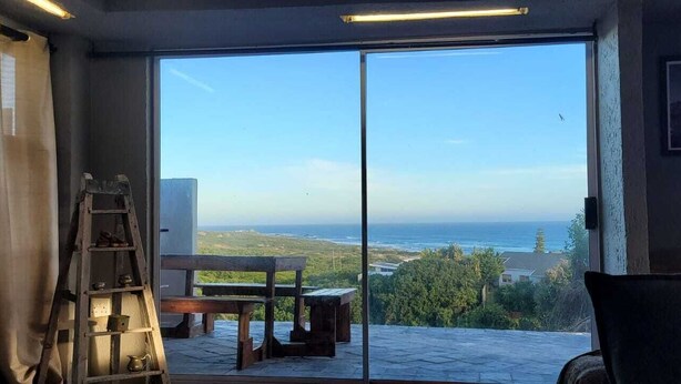 Quarto com grande porta de correr de vidro que dá para uma varanda com vista para o oceano e vegetação.