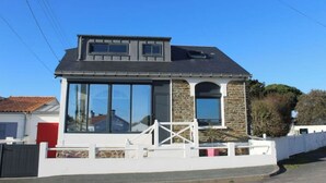 Een tweelaags huis met een gevel van natuursteen, grote ramen en een witte hekken.