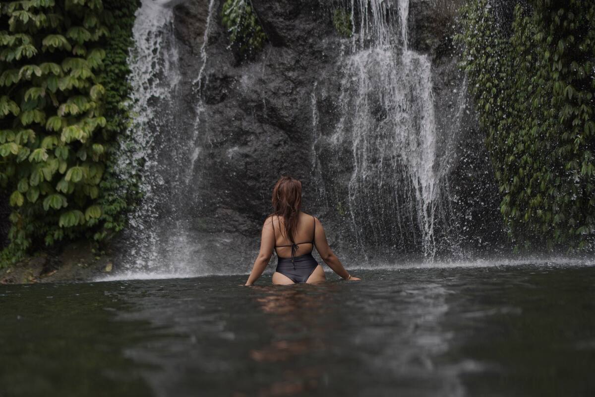 A person sitting in a body of water with a waterfall in the background.