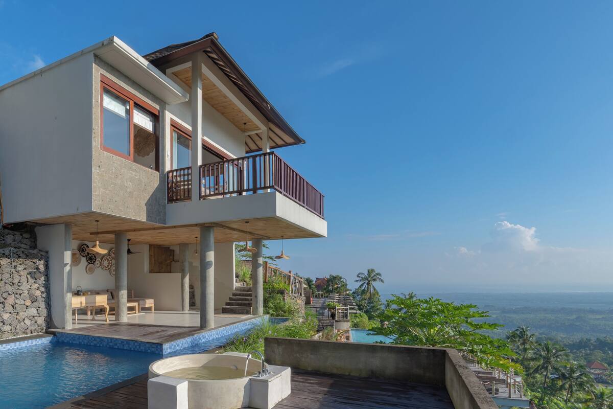 A modern two-story house with a balcony, a swimming pool, and a view of the landscape.