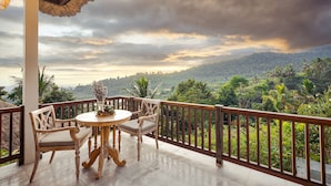 A balcony with a wooden table and chairs, overlooking a lush landscape with trees and hills. - Maha Hills Resort by Mahaprana Experience (Sukasada)