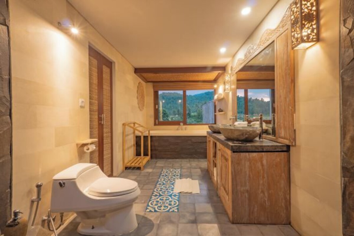Un baño con inodoro, lavabo de gran tamaño y zona de ducha, además de vistas al exterior a través de una ventana.