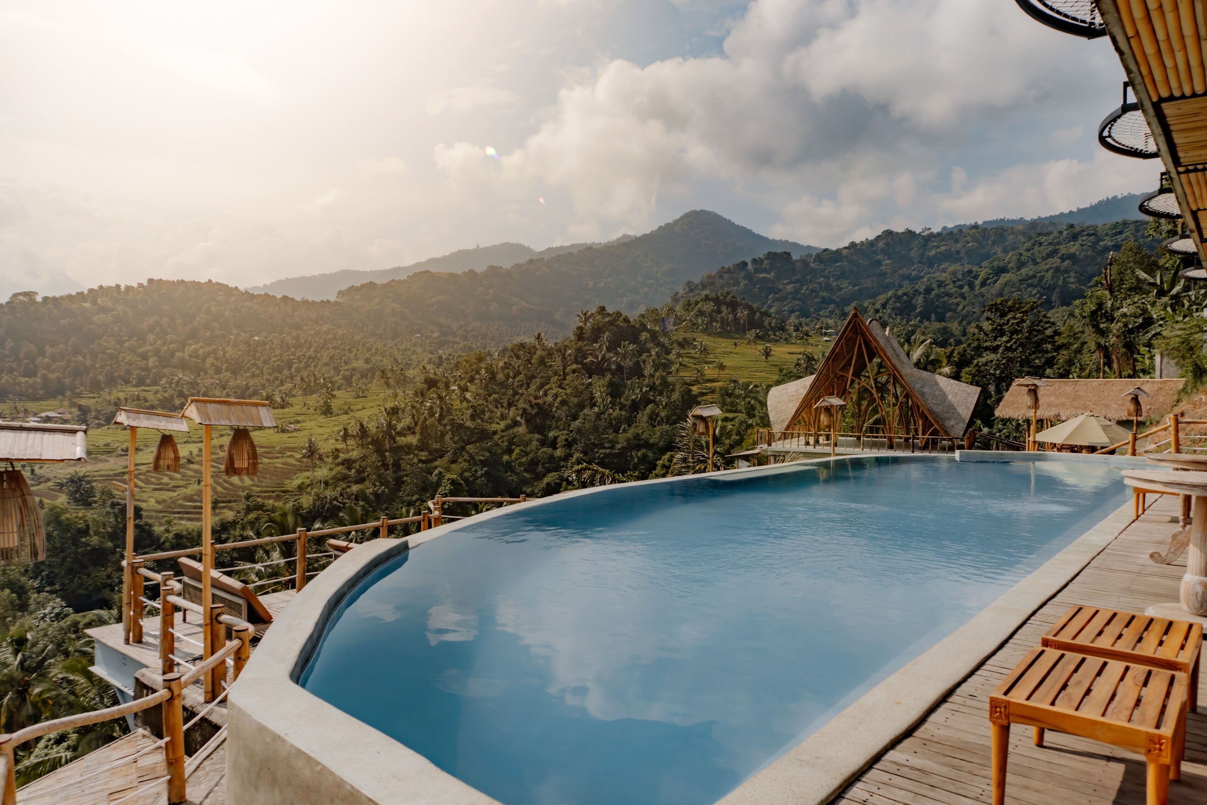 A pool with a wooden deck and a view of lush green hills and mountains in the background.