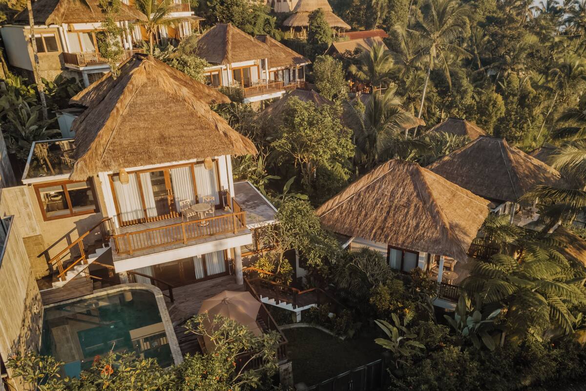 A resort with multiple thatched-roof villas, a swimming pool, and lush tropical vegetation.