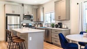A modern kitchen with grey cabinets, stainless steel appliances, a central island, and blue bar stools. - LOVELY STAY |GREAT LOCATION NEAR DISNEY & DOWNTOWN (Fullerton)