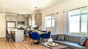 A modern kitchen with a central island, dining area with blue chairs, and a grey sofa by a large window. - LOVELY STAY |GREAT LOCATION NEAR DISNEY & DOWNTOWN (Fullerton)