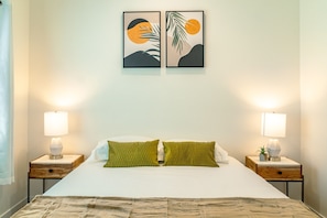 Ein ordentlich bezogenes Bett mit zwei Kissen, zwei Nachttischen mit Lampen und zwei gerahmten Kunstwerken an der Wand.