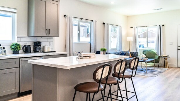 A modern kitchen with a central island, bar stools, and a dining area with a sofa and table. - LOVELY STAY |GREAT LOCATION NEAR DISNEY & DOWNTOWN (Fullerton)