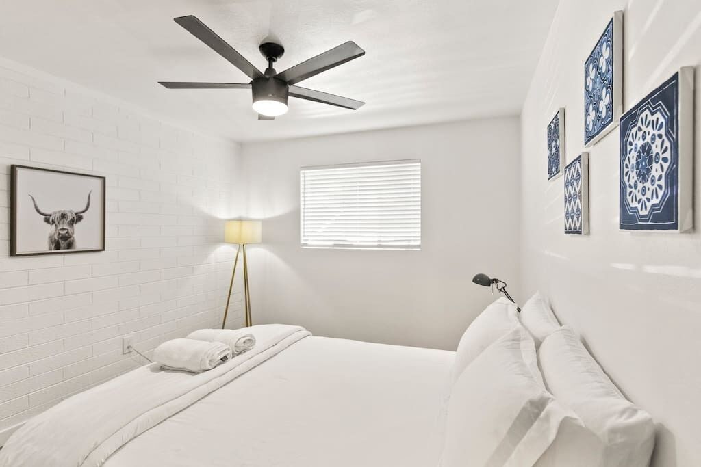 A bedroom with a bed, a ceiling fan, a lamp, and decorative wall art.