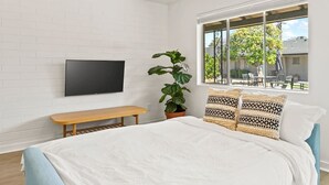 A bedroom with a bed, a bench, a TV mounted on the wall, a potted plant, and a window with a view of the outside. - Lovely 1-bedroom condo in Baltimore - Parking (Phoenix)