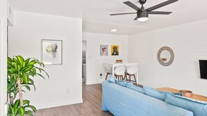 A modern living room with a blue sofa, a dining area with a table and chairs, a ceiling fan, and a wall-mounted TV. - Lovely 1-bedroom condo in Baltimore - Parking (Phoenix)