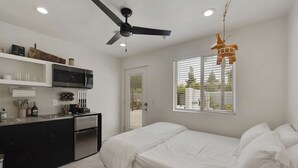A compact bedroom with a bed, a ceiling fan, a window with blinds, and a kitchenette with a microwave and refrigerator. - Hinny's sweet suite w/ Heated Pool, GYM & Hot Tub (Scottsdale)