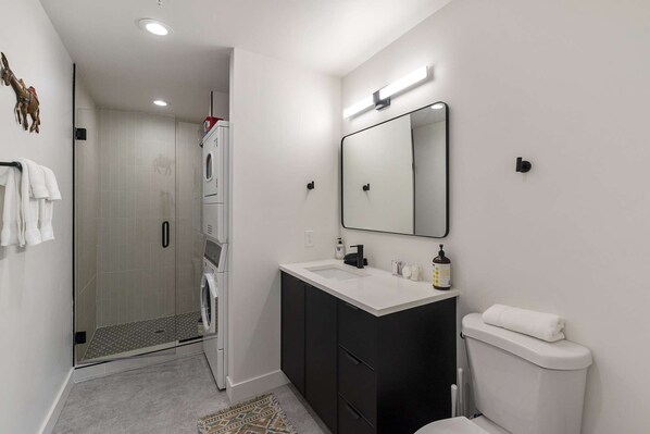A modern bathroom with a glass shower, a white sink, a black cabinet, and a toilet.
