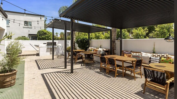 An outdoor patio with wooden tables and chairs, a grill, and string lights. - Hinny's sweet suite w/ Heated Pool, GYM & Hot Tub (Scottsdale)