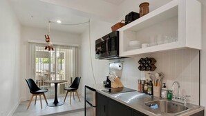 A compact kitchen with a microwave, sink, and storage shelves. There is a dining area with a table and chairs. - Cuddy's sweet suite W/ Heated Pool, GYM & Hot Tub (Scottsdale)