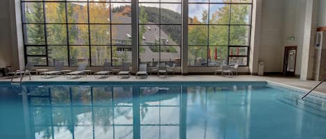 Une piscine intérieure offrant une vue dégagée sur un paysage montagneux grâce à de grandes fenêtres.