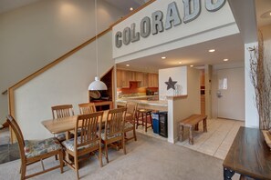 A dining area with a wooden table and chairs, a kitchen in the background, and a sign that reads "COLORADO". - Pines 2129 (Keystone)