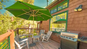 Una terraza de madera con mobiliario exterior, una parrilla y un gran paraguas.