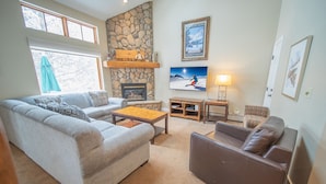 Una sala de estar con chimenea de piedra, un televisor de pantalla plana grande y un rincón de descanso acogedor con sofá y sillón de cuero marrón.