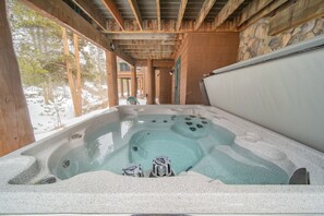 Un jacuzzi con pared de piedra y vigas de madera, rodeado de un paisaje nevado.