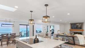 Una cucina moderna con isola centrale, illuminazione a sospensione e vista mare.