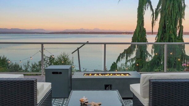 Un balcone con mobili in vimini, un braciere e vista su un lago e montagne.