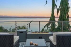 A balcony with wicker furniture, a fire pit, and a view of a lake and mountains. - Spacious 3-bedroom house with parking!!! (Camano)