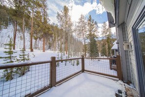 Um deck coberto de neve com guarda-corpo de madeira, rodeado por altas árvores de pinheiro.
