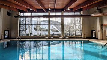 An indoor swimming pool with a view of snow-covered trees and buildings through large windows.