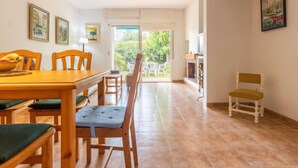 A dining area with a wooden table and chairs, a view of the garden through a glass door, and a painting on the wall. - Vacation home Boters by Interhome (Torredembarra)