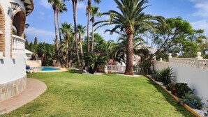 A well-maintained lawn with a pool, surrounded by tall palm trees and a white building with a curved balcony.