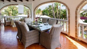 A dining area with wicker furniture, a glass table, and a view of palm trees.