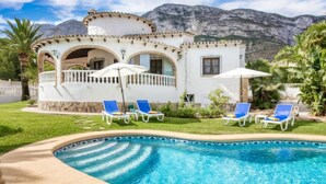 A poolside area with a pool, blue lounge chairs, and a building with arches and a balcony.