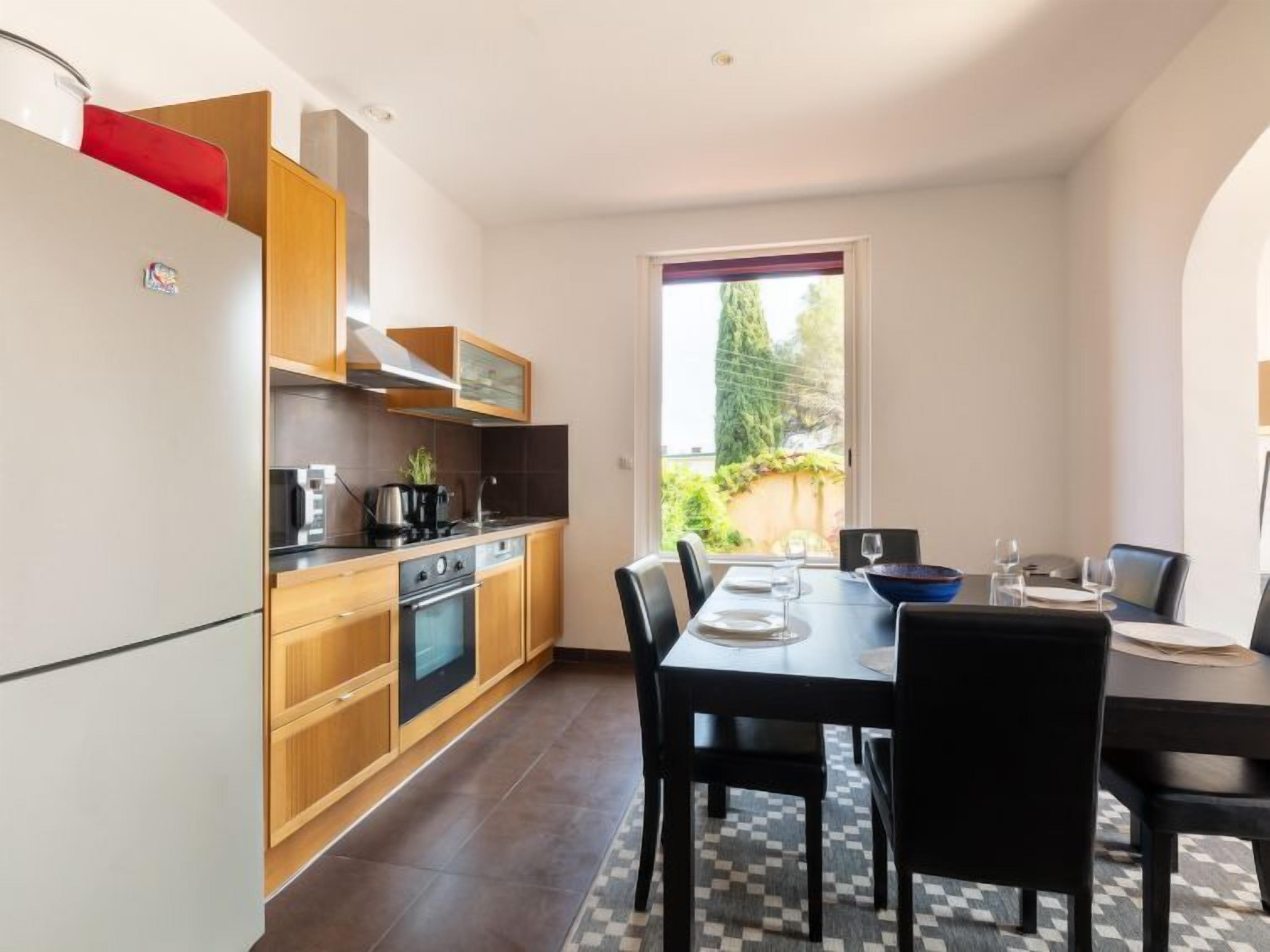A modern kitchen with wooden cabinets, a built-in oven, and a dining area with a checkered floor rug.