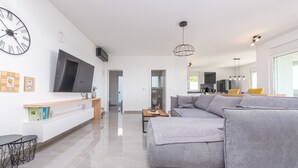 A modern living room with a grey sofa, a flat-screen TV, a wooden console table, and a large clock on the wall. - Villa Suton (Razanac)