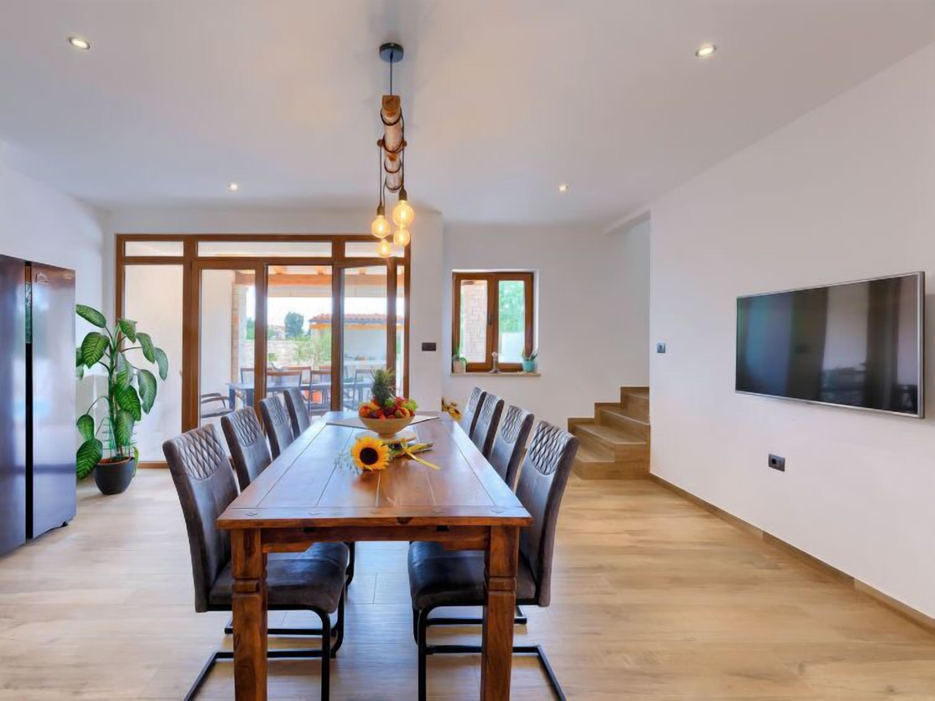 A modern dining area with a wooden table, leather chairs, a fruit bowl, and a unique pendant light.