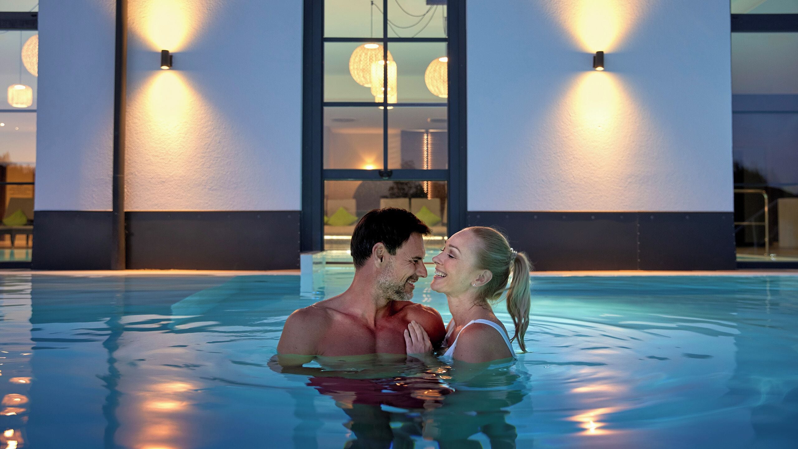 Um casal em uma piscina com um edifício moderno ao fundo.