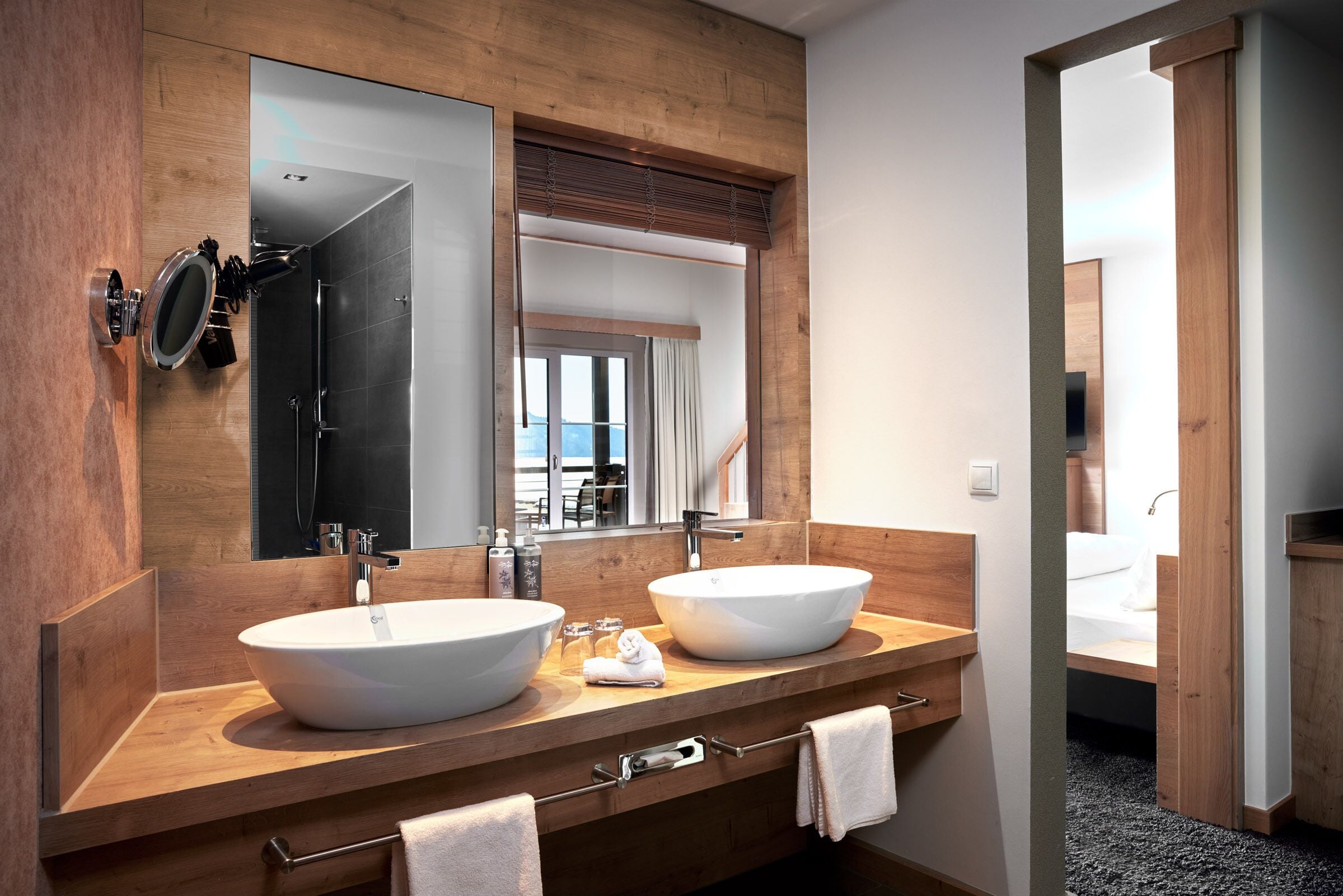 A modern bathroom with two large sinks, a mirror, and a view of a bedroom.