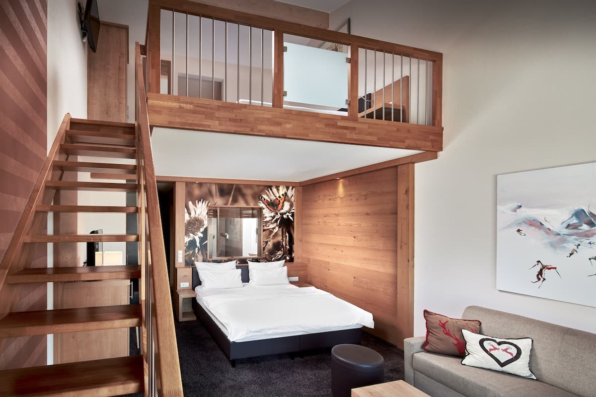Een slaapkamer met een bed in loftstijl, een houten trap, een bank met kussens, en een schilderij aan de muur.