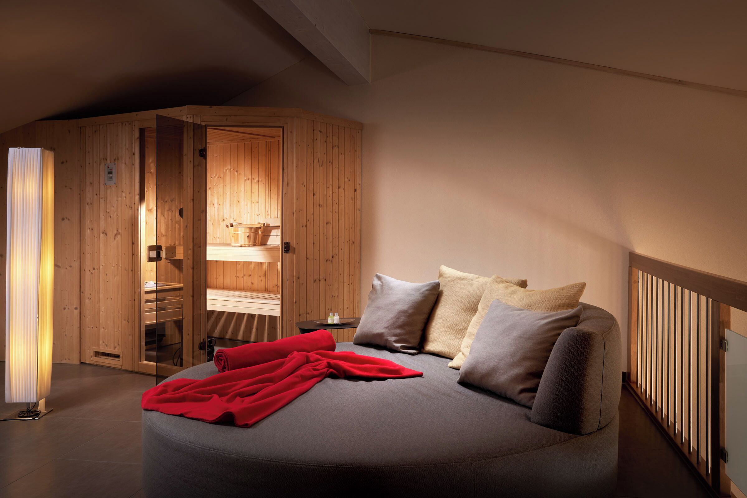 A cozy bedroom with a bed, pillows, a red blanket, a wooden wardrobe, and a nightstand.