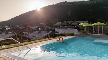 Una piscina con vista a casas de madera tradicionales y una colina boscosa al fondo.
