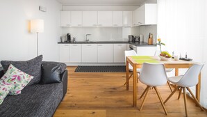 Moderni keittiö, jossa on valkoiset kaapit, ruokapöytä ja kaksi tuolia sekä kukkapuvukuvioitu koristetyyny sohvan päällä.