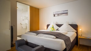 Moderni hotellihuone, jossa on suuri sänky, yöpöytä lampun kanssa, penkki ja ikkunasta avautuva merinäköala.